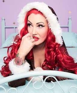 BellaX reclining on a light blue bed frame with red hair and soft studio lighting, representing tantric massage, embodied touch therapy, and sensual wellness services