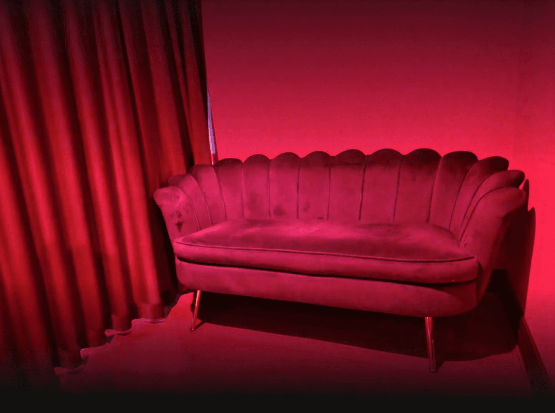 Red velvet lounge sofa in a softly lit sensual massage room at Luxxx Erotic Massage in Melbourne