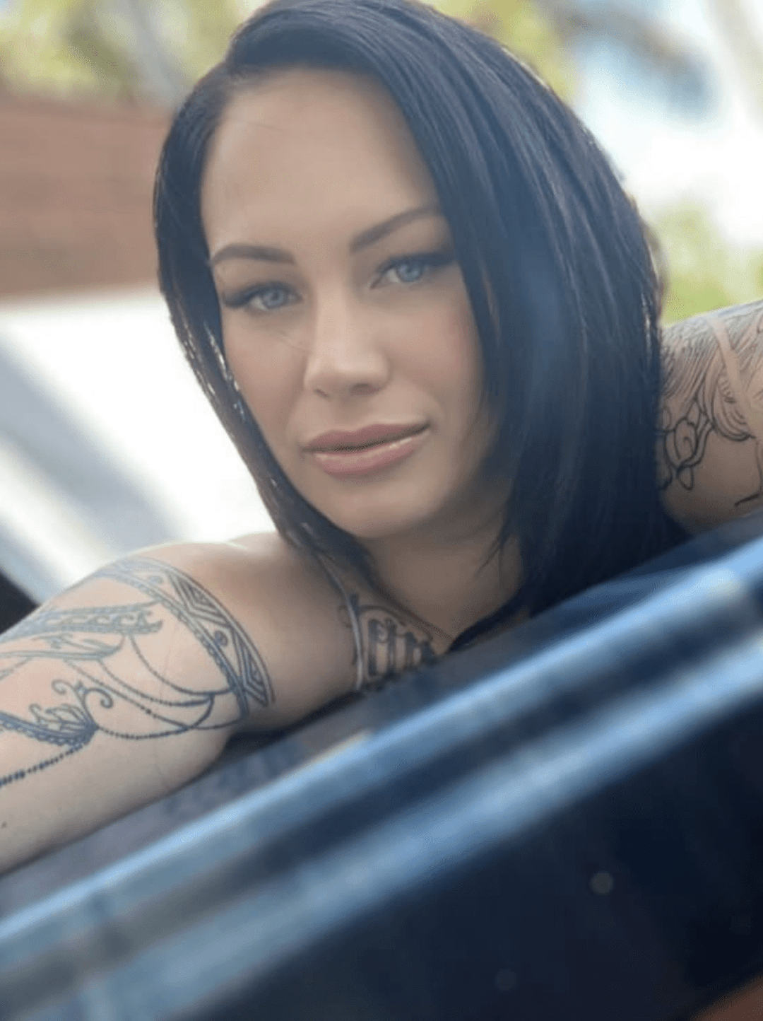 Lexi Love independent erotic massage provider with dark hair and arm tattoos, featured profile image taken outdoors in natural light.